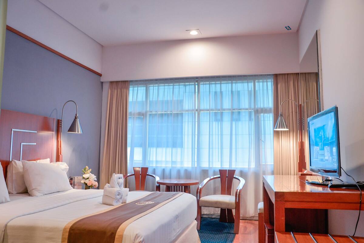 A hotel room with a large bed, a desk with a computer, a chair, and a TV.