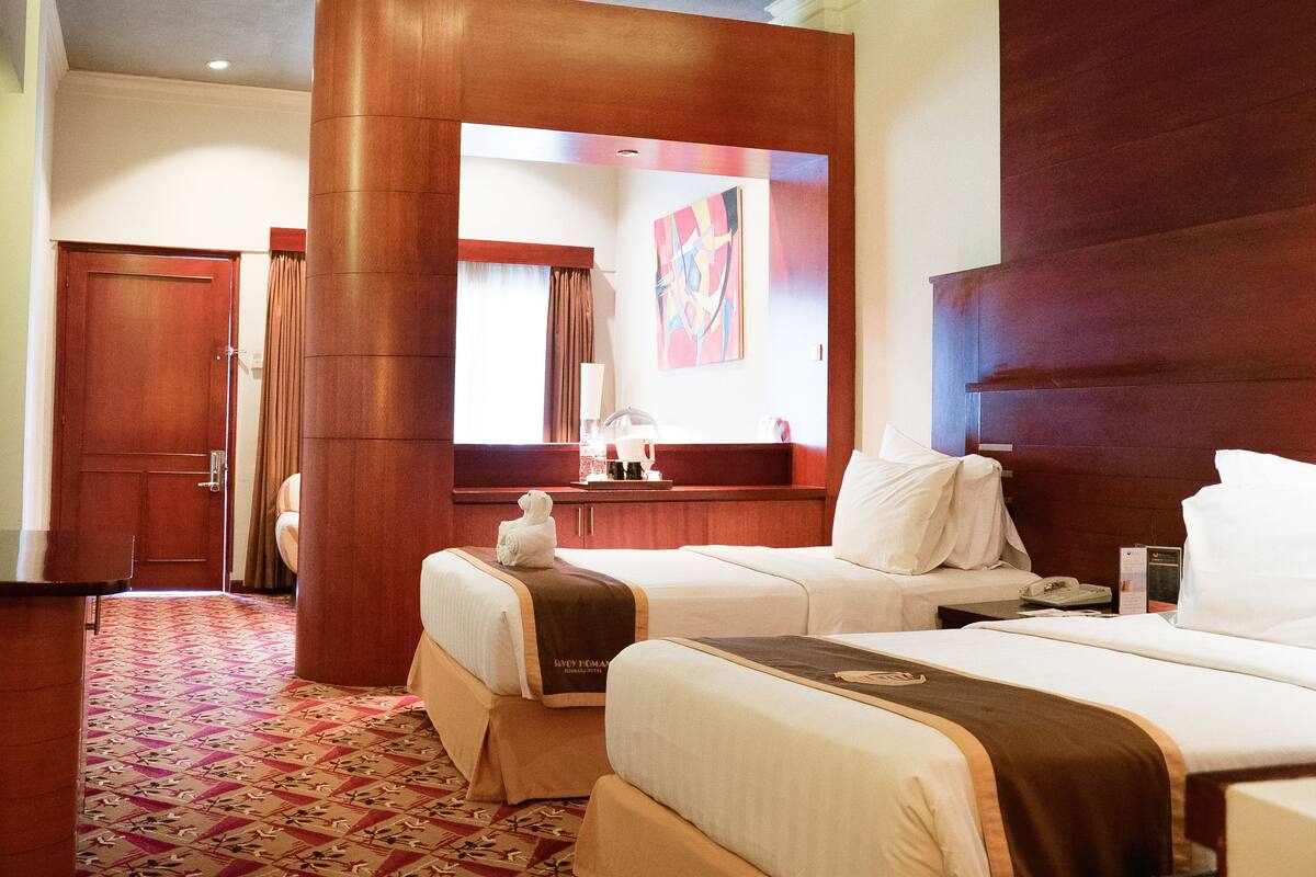 A hotel room with two beds, a wooden headboard, a flat-screen TV, a large mirror, and a patterned carpet.