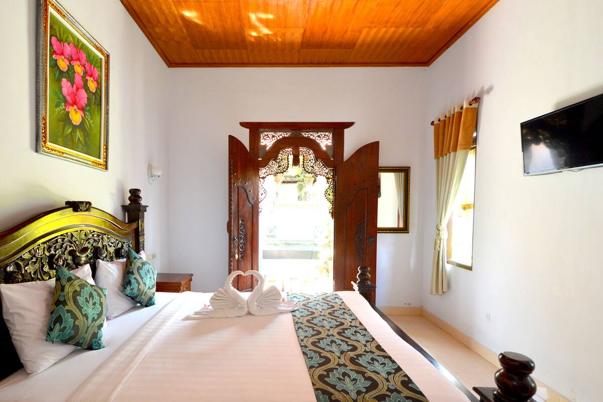A hotel room with a large bed, a wooden headboard, a painting on the wall, and a television.