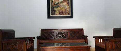 Una habitación con un sofá de madera y dos sillones, una mesa de centro de cristal y un cuadro enmarcado en la pared.