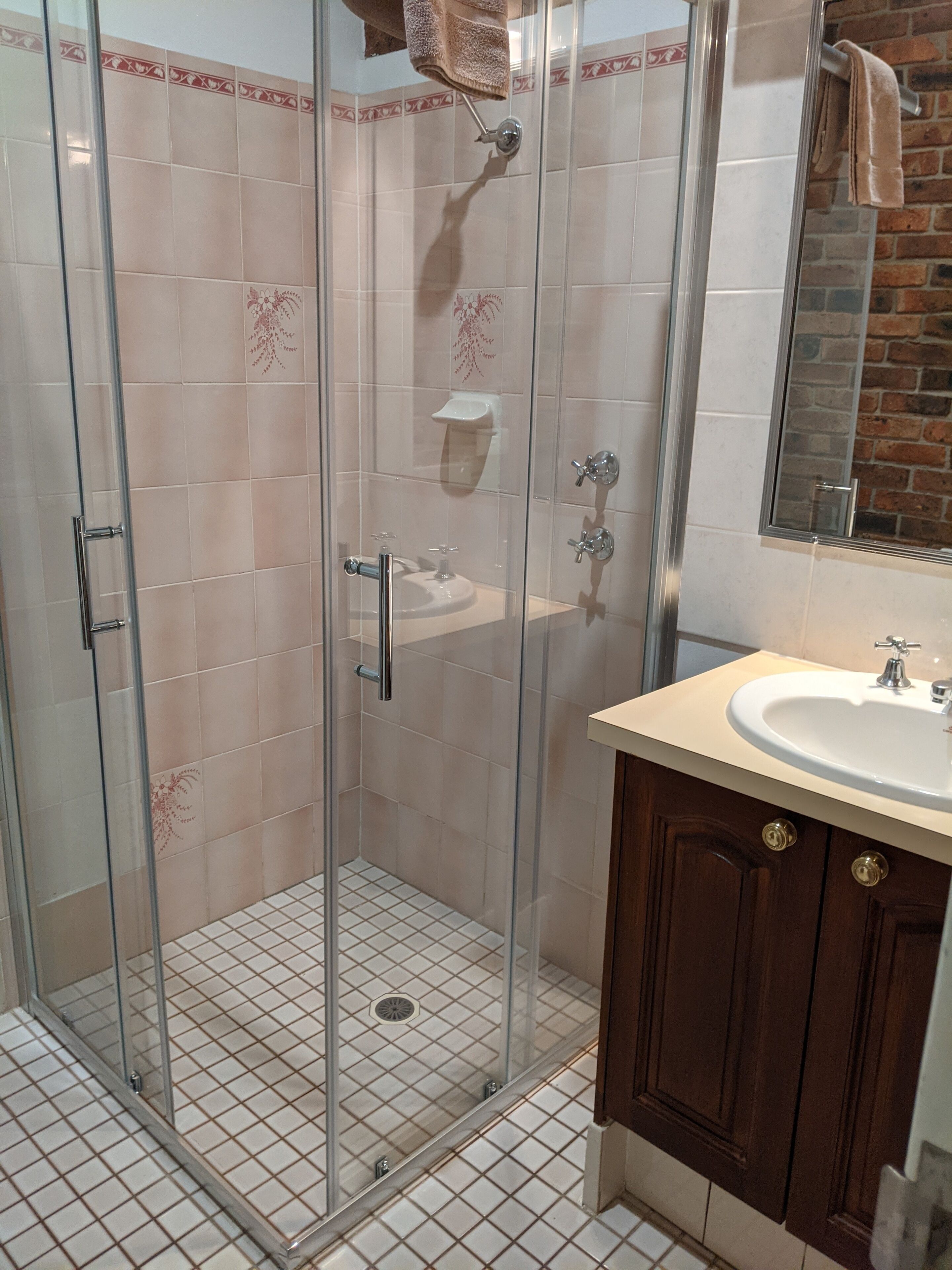 A glass-enclosed shower with a tiled floor, a sink, and a mirror above it.
