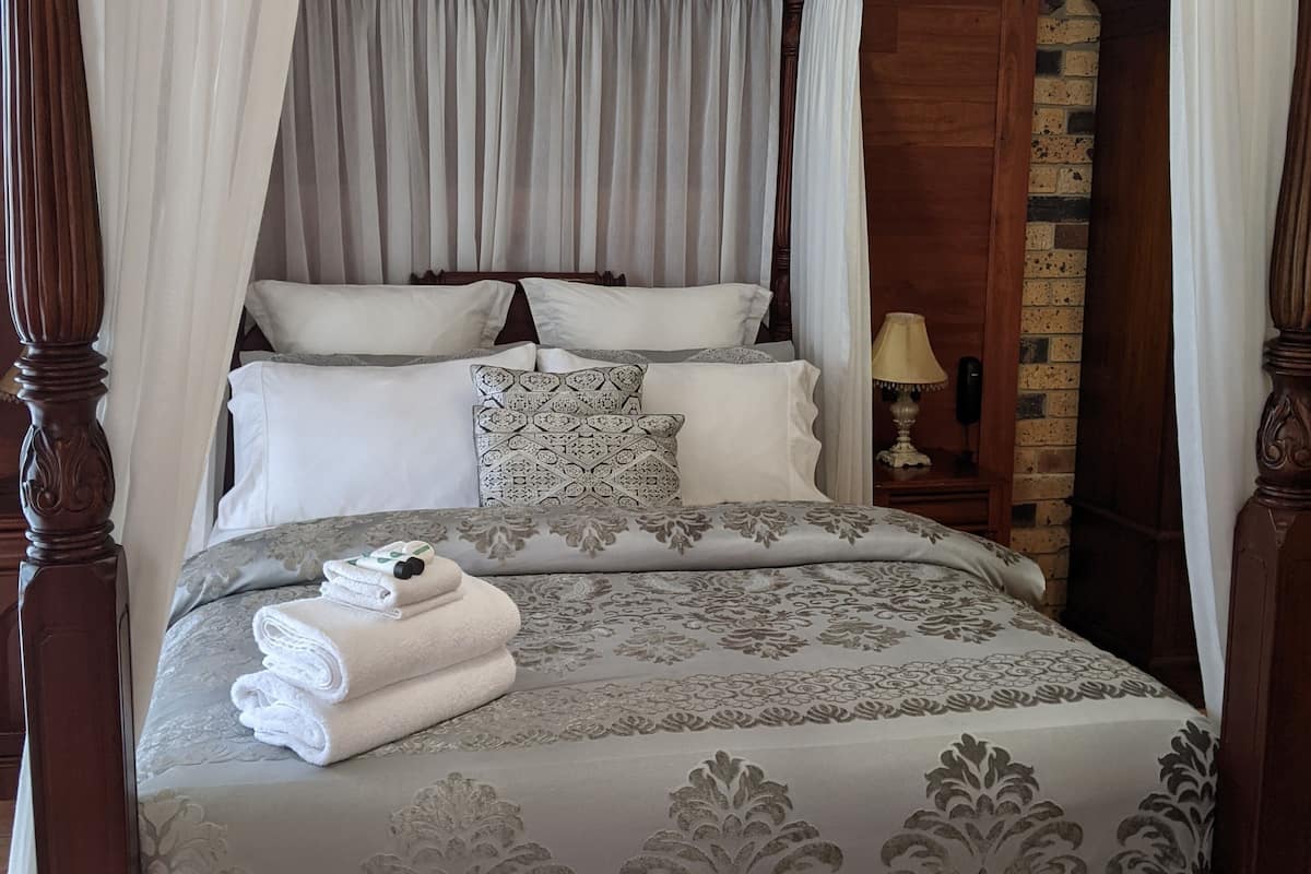 Un lit à baldaquin à quatre poteaux, avec une couvre-lit à motifs gris et blancs, des oreillers blancs et une serviette blanche pliée posée sur le côté.