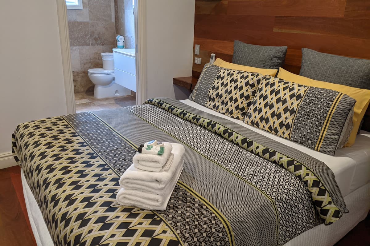 Une chambre d’hôtel avec un grand lit, une tête de lit en bois et une salle de bain visible à travers une porte ouverte.