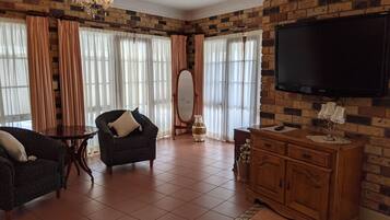 A living room with a brick wall, a chandelier, a TV, and a wooden cabinet.