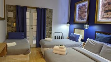 Habitación de hotel con dos camas, una pared de piedra, una puerta con cortinas e imágenes enmarcadas.