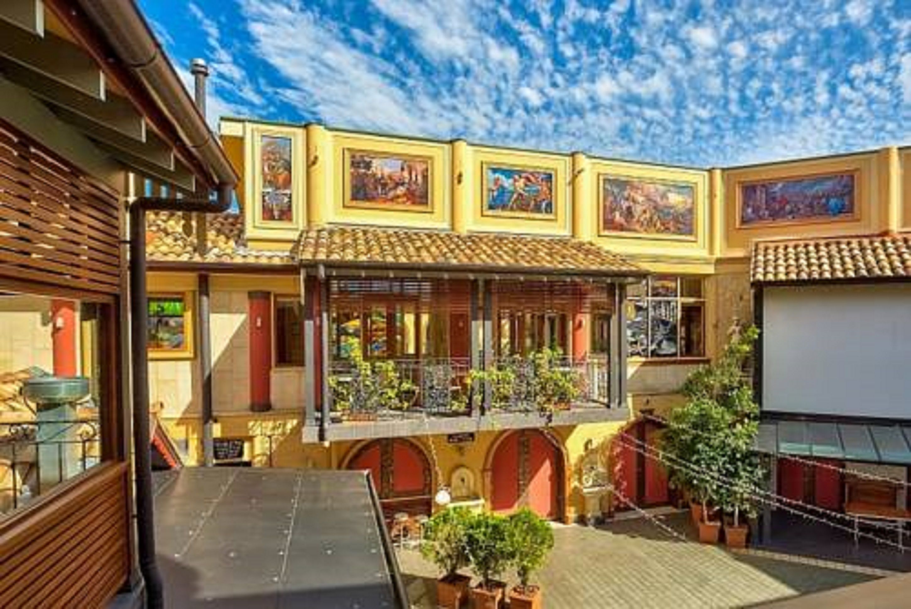 A courtyard with a covered seating area, potted plants, and a building with a tiled roof and murals.