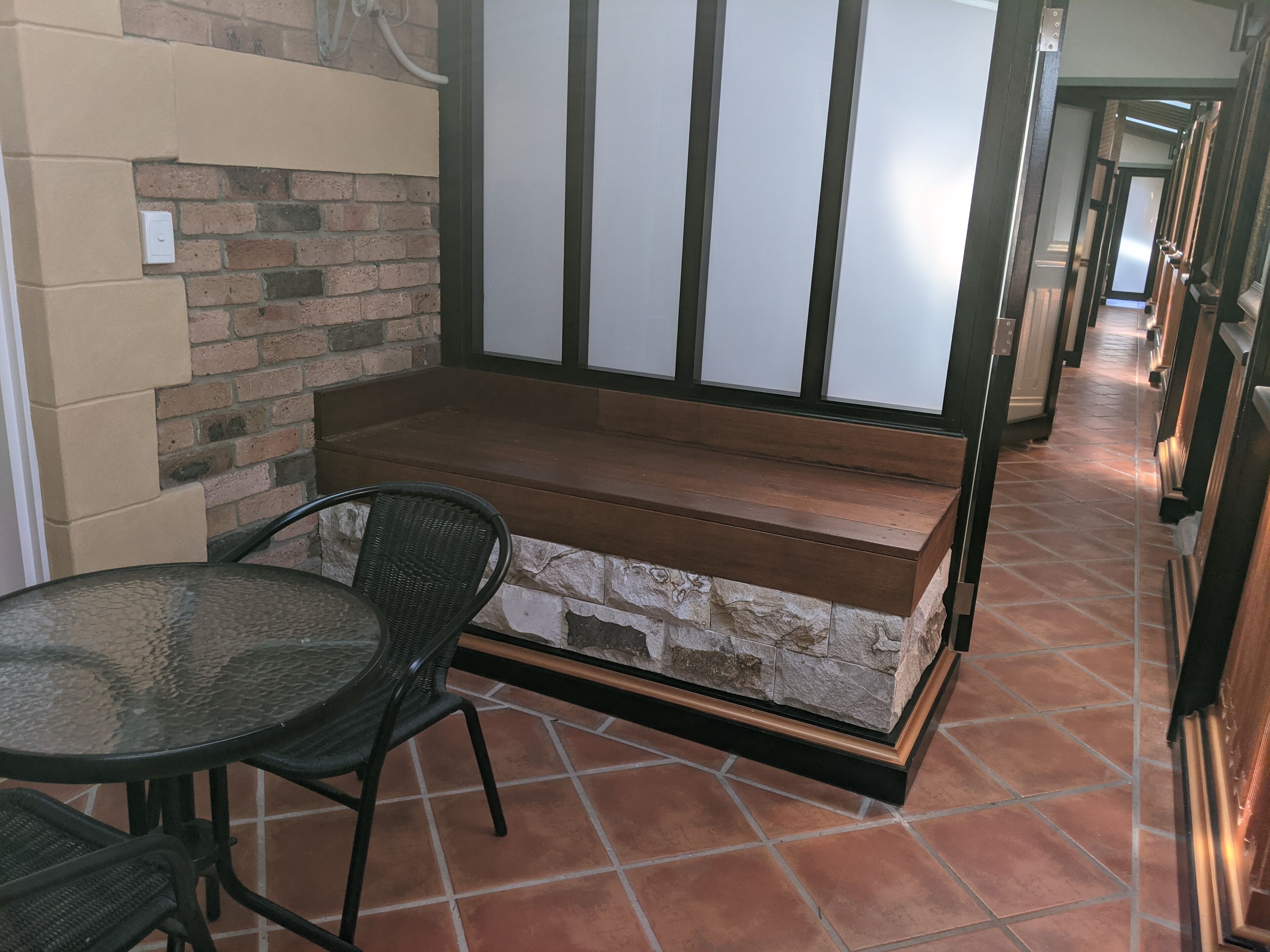 Een gang met een stenen bank, een glazen tafel en stoelen.