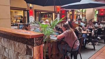 An outdoor dining area with wooden tables and black umbrellas, surrounded by stone walls and potted plants.