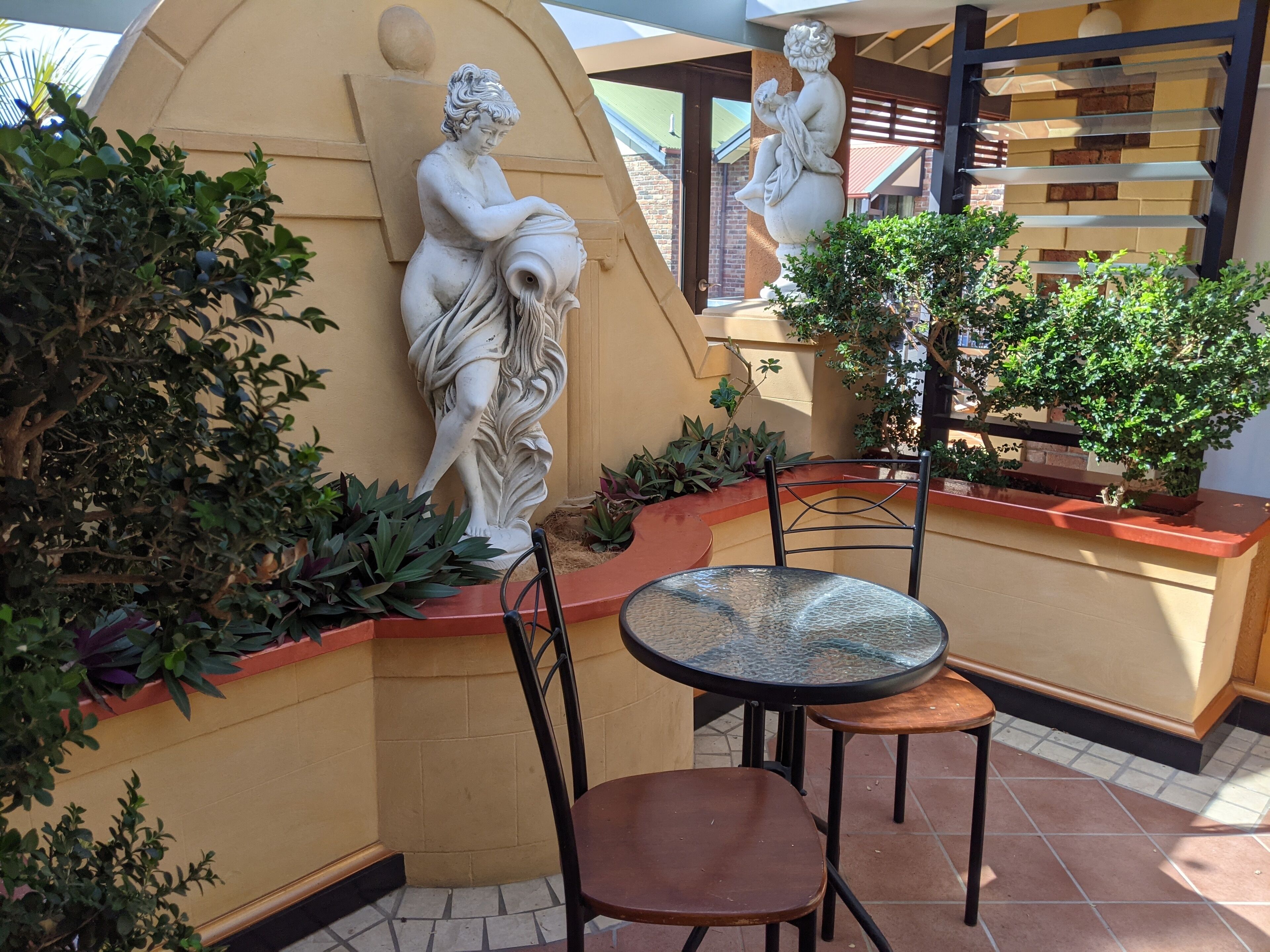 A patio area with a statue of a woman, a round table, and chairs.