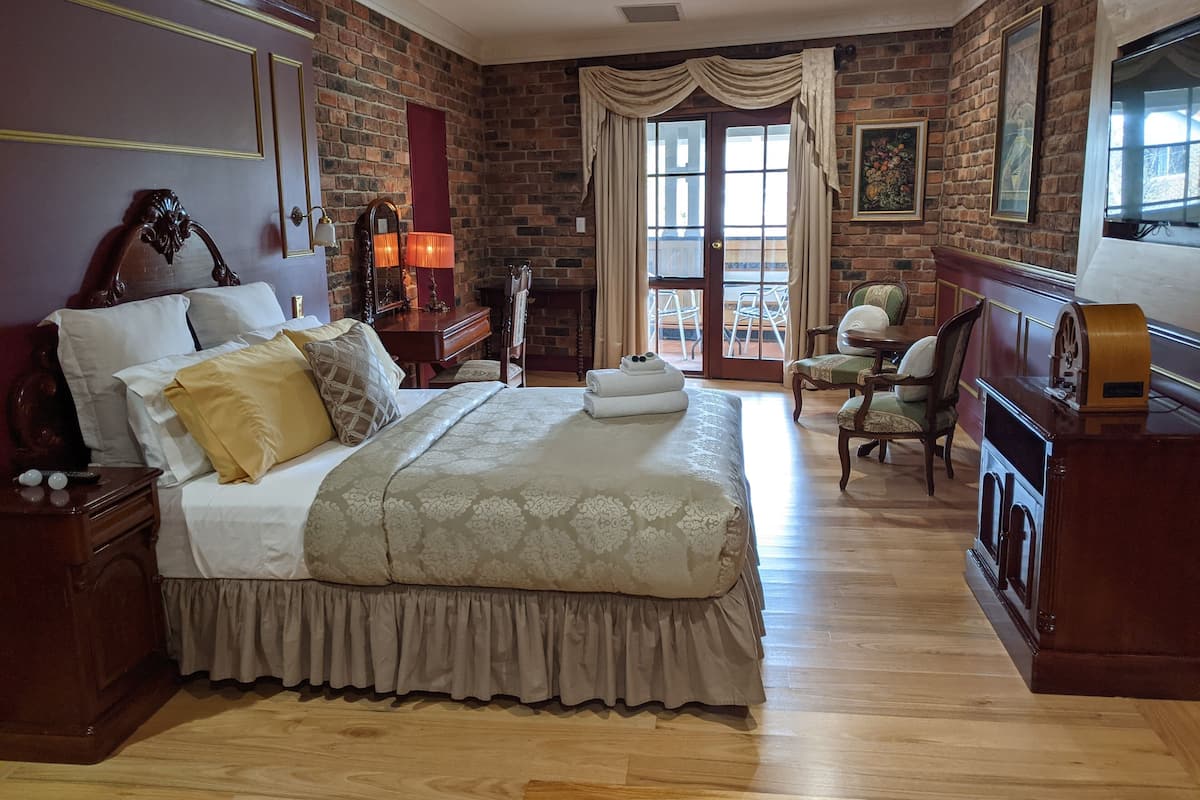 Une chambre d’hôtel avec un grand lit, des meubles en bois, une cheminée et un balcon équipé de chaises.