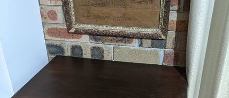 A dark wooden table with a chair in front of a brick wall with a framed sign that reads "Calligraphy Lessons."