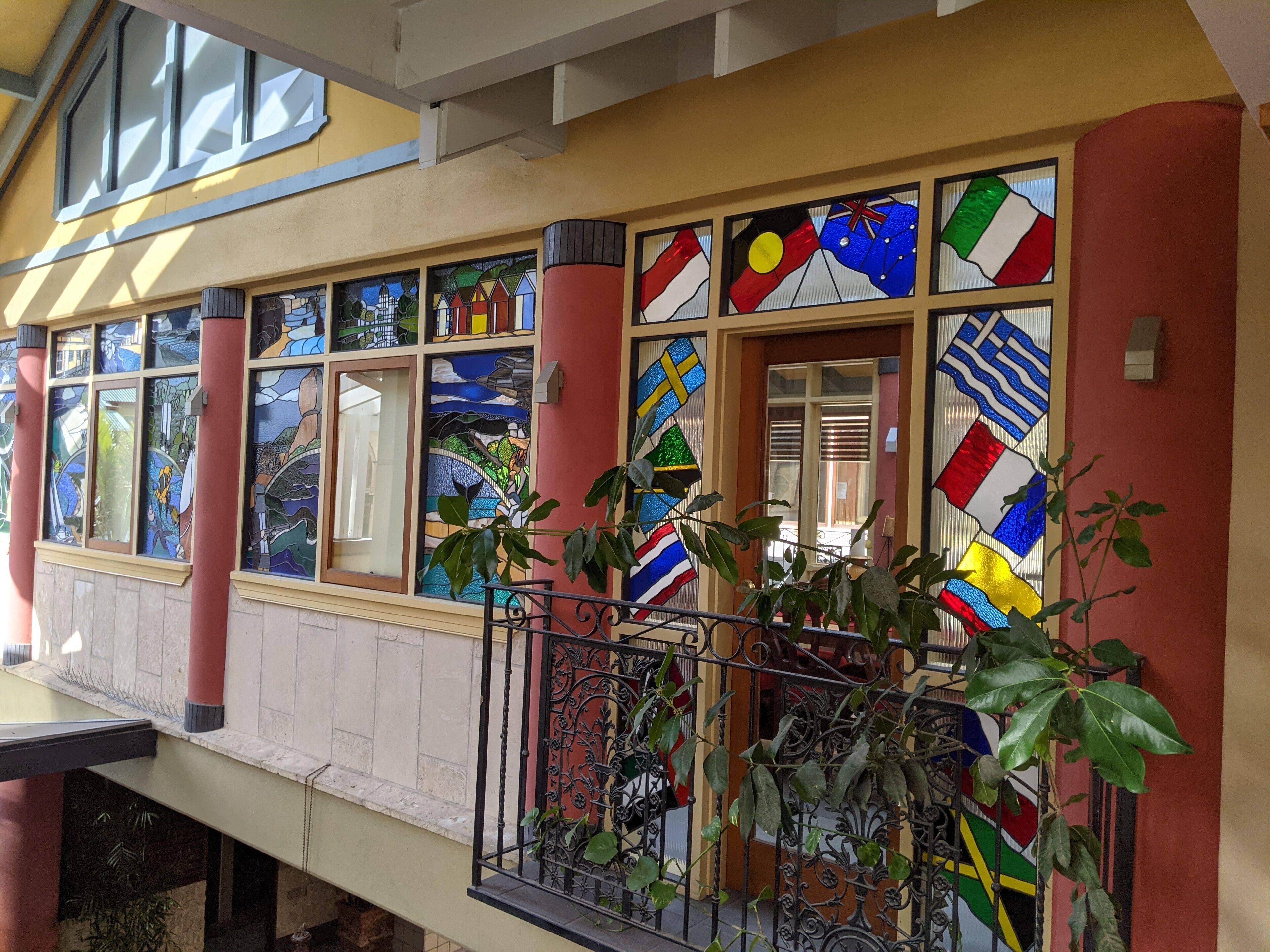 Fachada de edificio con vidrieras de colores, un balcón con barandillas de metal y plantas en macetas.