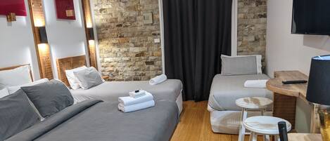 Ein Hotelzimmer mit zwei Betten, einer Steinwand, einem Flachbildfernseher und einem kleinen Tisch mit einer Lampe.