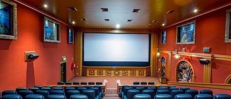 Een theater met rijen blauwe zitplaatsen, een groot scherm en ingelijste kunstwerken aan de muren.