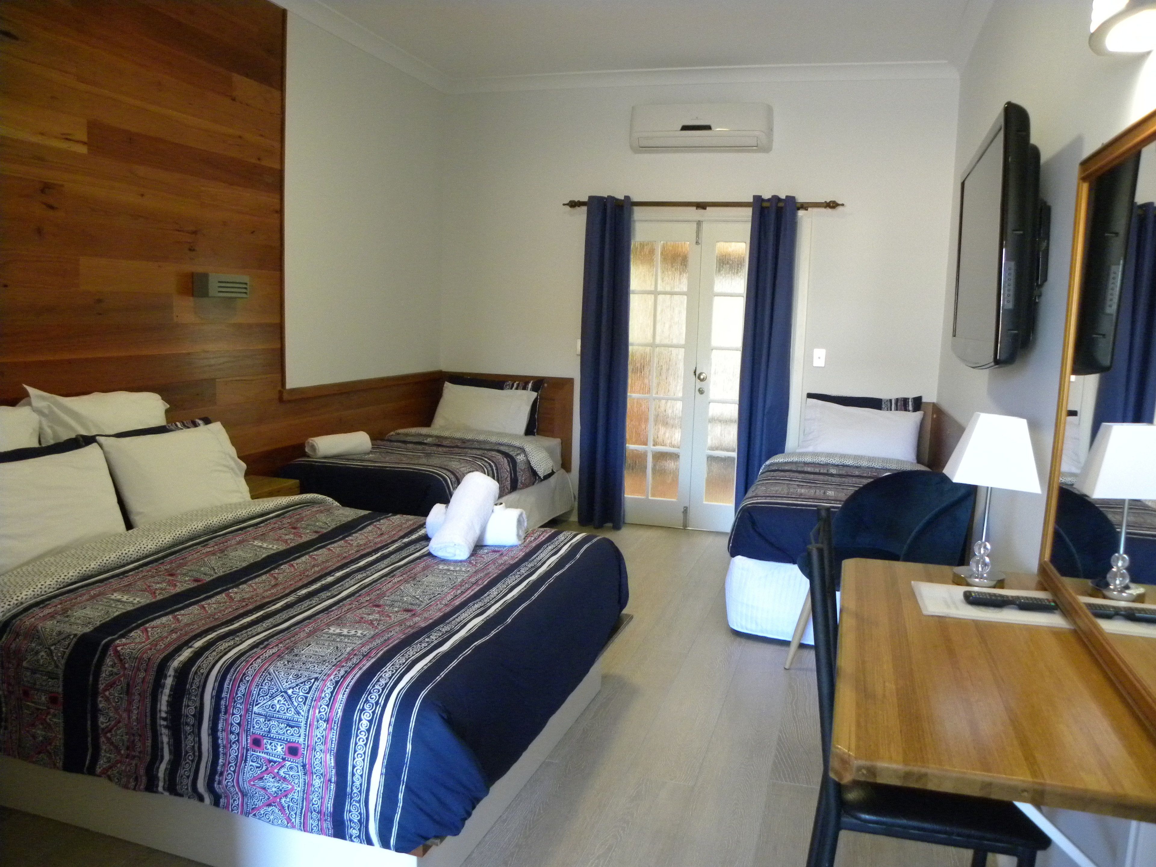 A hotel room with two beds, a wooden headboard, a desk with a chair, a mirror, and a television.