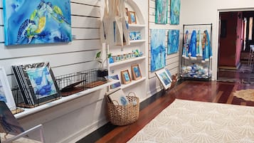 Galleriaa muistuttava huone, jossa on puulattia, valkoiset seinät ja erilaisia taideteoksia esillä hyllyillä ja seinillä.