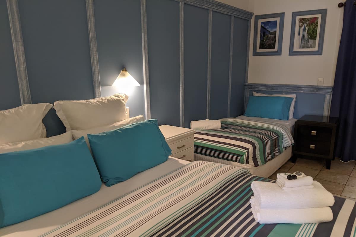 Une chambre d’hôtel avec deux lits, chacun agrémenté de draps à rayures et d’oreillers turquoise. Une table de chevet avec une lampe se trouve entre les deux lits.