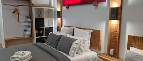A modern hotel room with a large bed, a wooden headboard, a red accent wall, and built-in shelving.