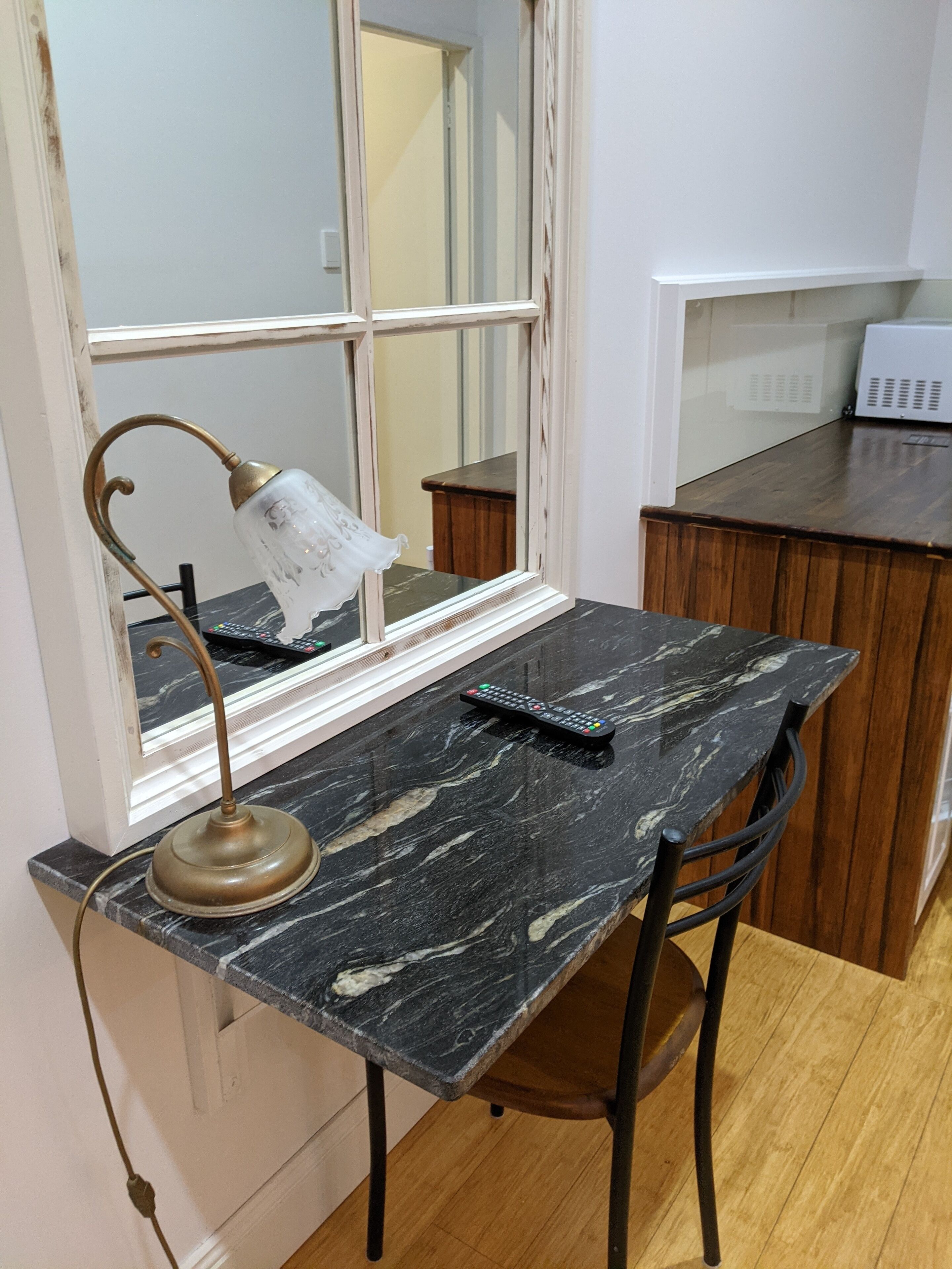 Une petite cuisine avec un plan de travail en marbre, une chaise en bois, une lampe de table et un four à micro-ondes.