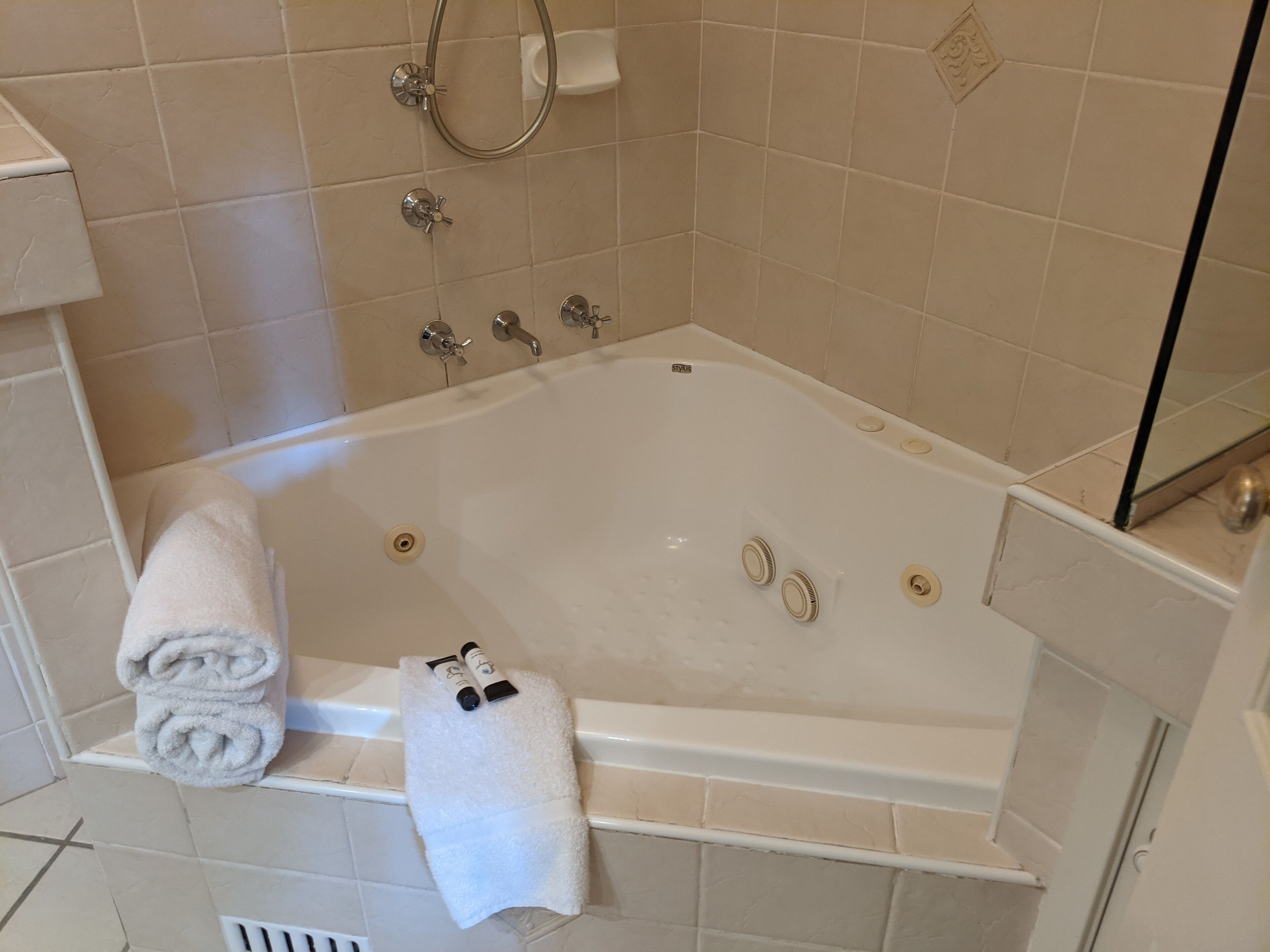 Una bañera blanca con ducha, dos grifos y un desagüe. Hay dos toallas y dos botellas en el borde de la bañera.
