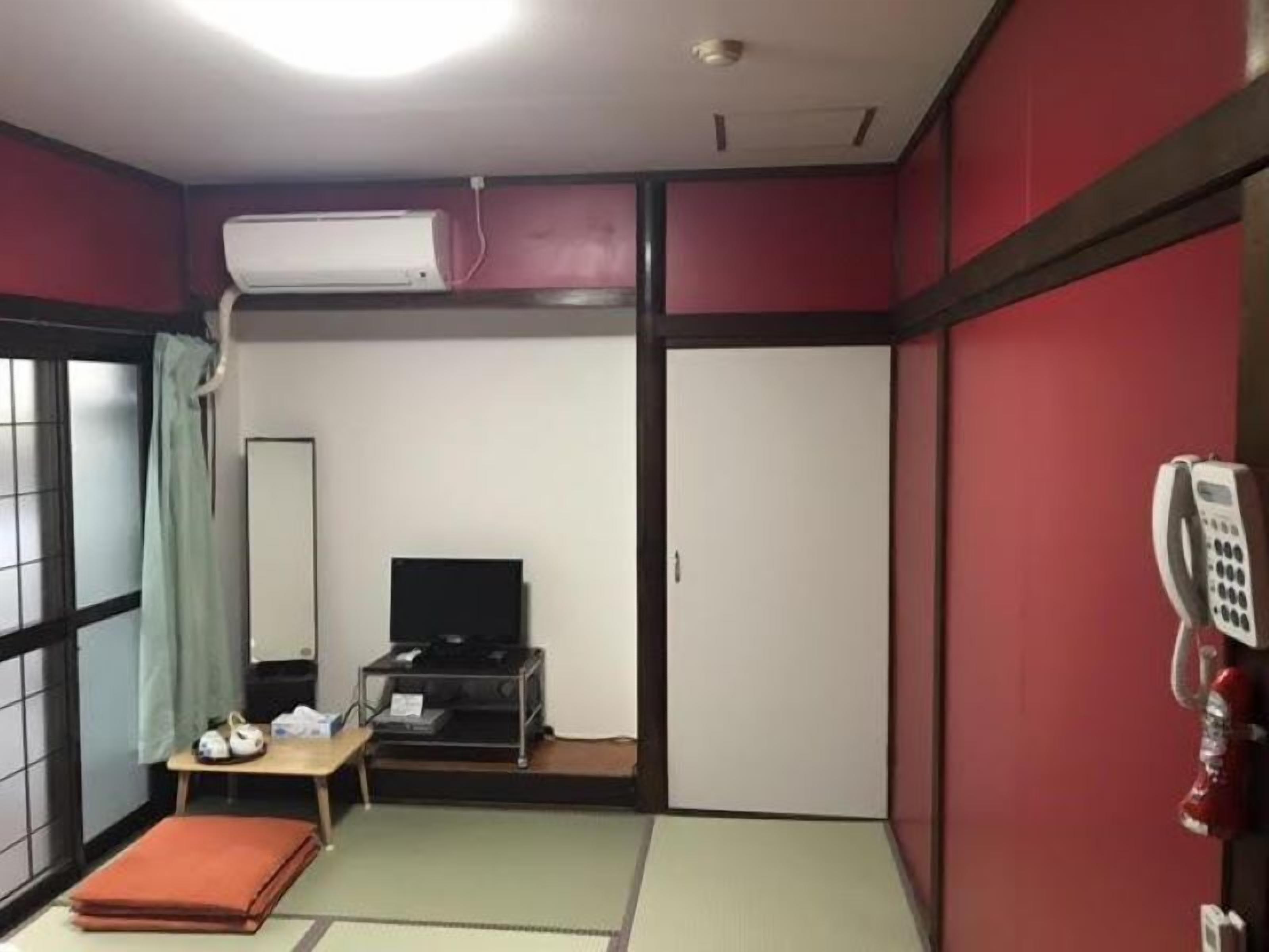 A small hotel room with a bed, a desk with a chair, a television, and a telephone.