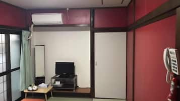 A small hotel room with a bed, a desk with a chair, a television, and a telephone.
