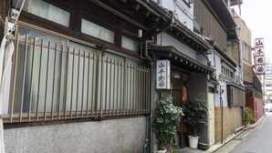 A traditional Japanese building with a wooden fence, potted plants, and a sign with Japanese characters.