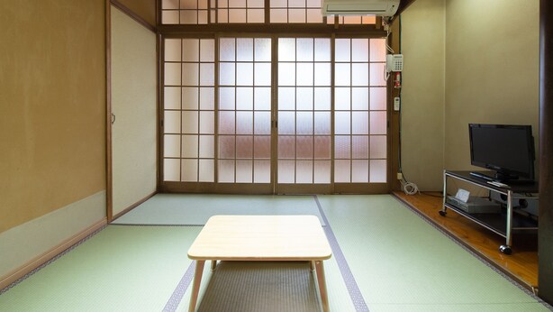 A traditional Japanese room with tatami flooring, a sliding shoji door, a television on a stand, and a small table.