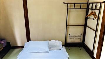 A traditional Japanese room with tatami flooring, a low bed with a white and black patterned blanket, and a wooden wardrobe with a hanging rack.