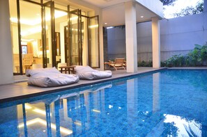 A swimming pool with loungers and a glass door leading to a room.