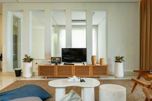 A modern living room with a flat-screen TV, wooden entertainment unit, and two potted plants.