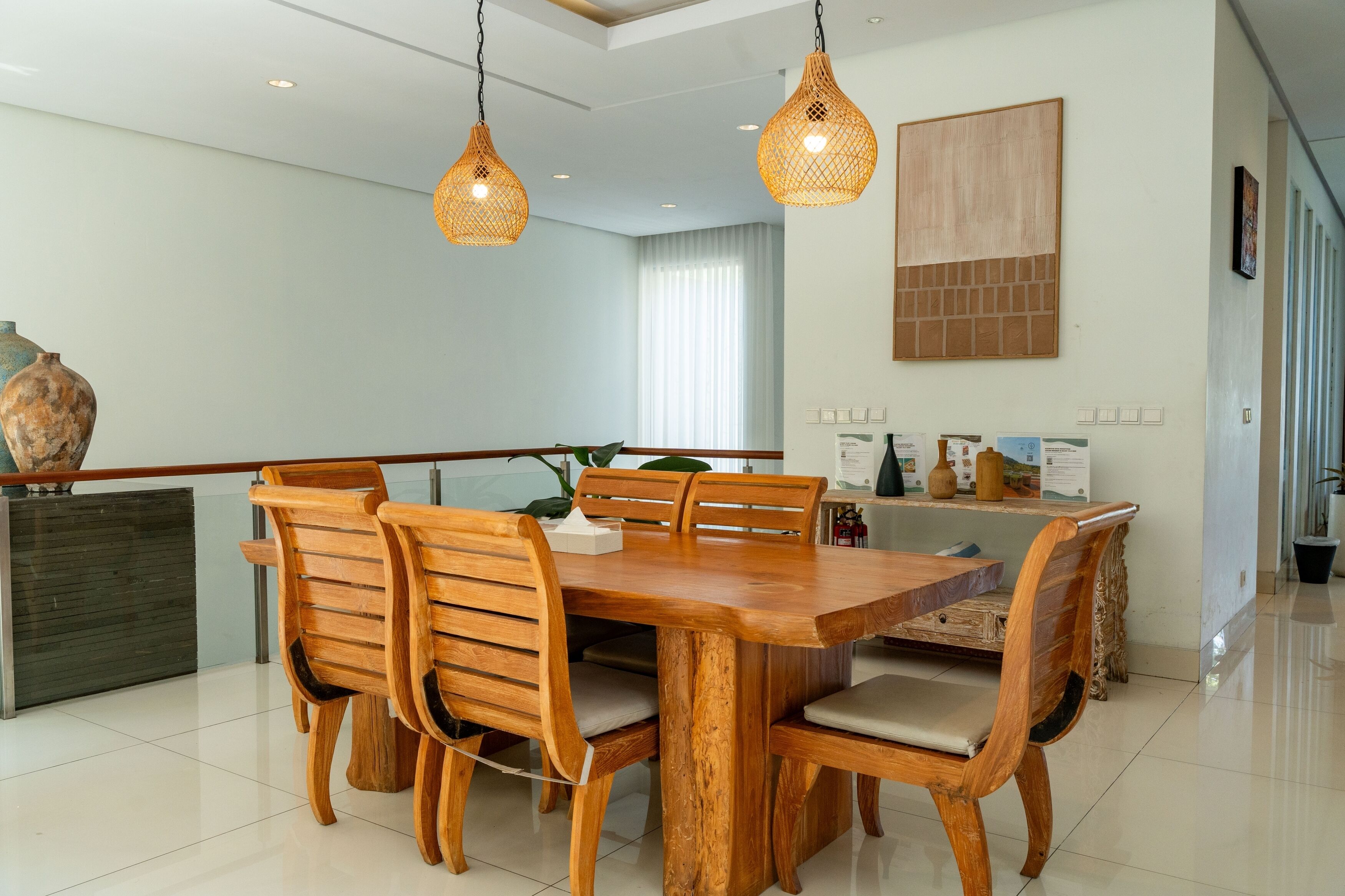 A dining area with a wooden table and chairs, pendant lights, a vase, and a window with curtains.