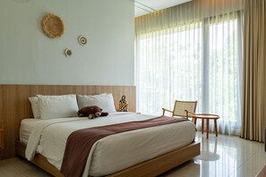 A hotel room with a large bed, a bedside table, a chair, and a view of the outdoors through sheer curtains.
