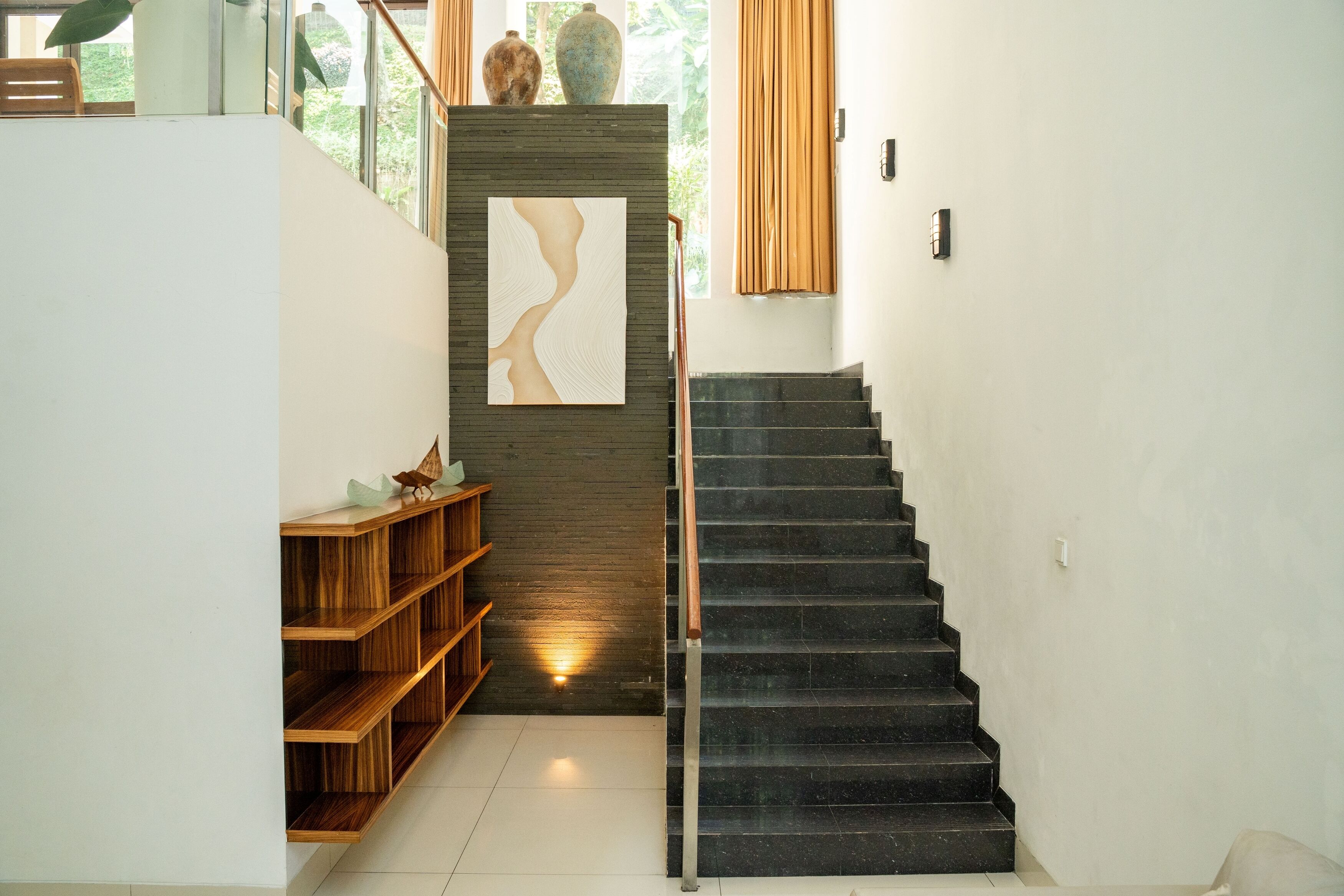 A modern staircase with a wooden shelf and a decorative wall piece.