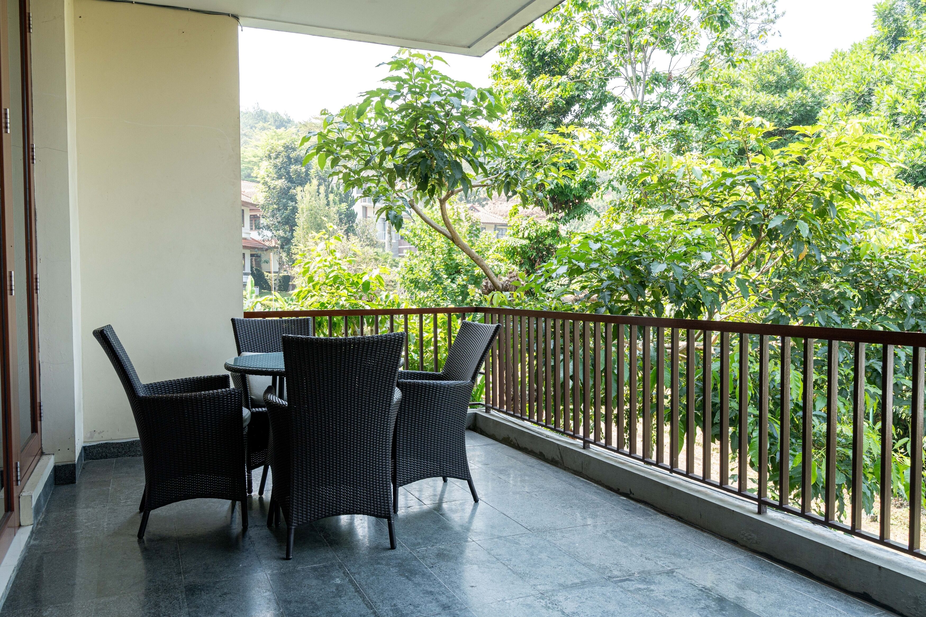 Un balcón con mesa y sillas, barandilla y vistas a árboles y edificios.