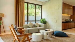 Ein modernes Wohnzimmer mit einer Couch, Sesseln, einem Couchtisch und einem durchgehenden Gang sichtbarem Küchenbereich.