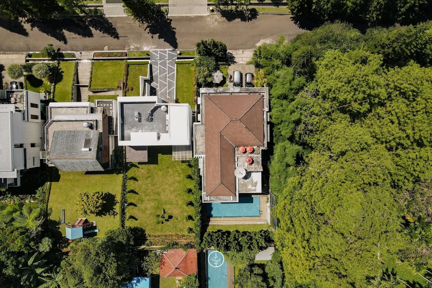 Vue aérienne d’un bâtiment moderne doté d’une piscine, entouré d’une végétation luxuriante et d’un espace de stationnement.