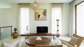 Un salon moderne avec une table basse en bois, un canapé, un téléviseur et un luminaire suspendu.