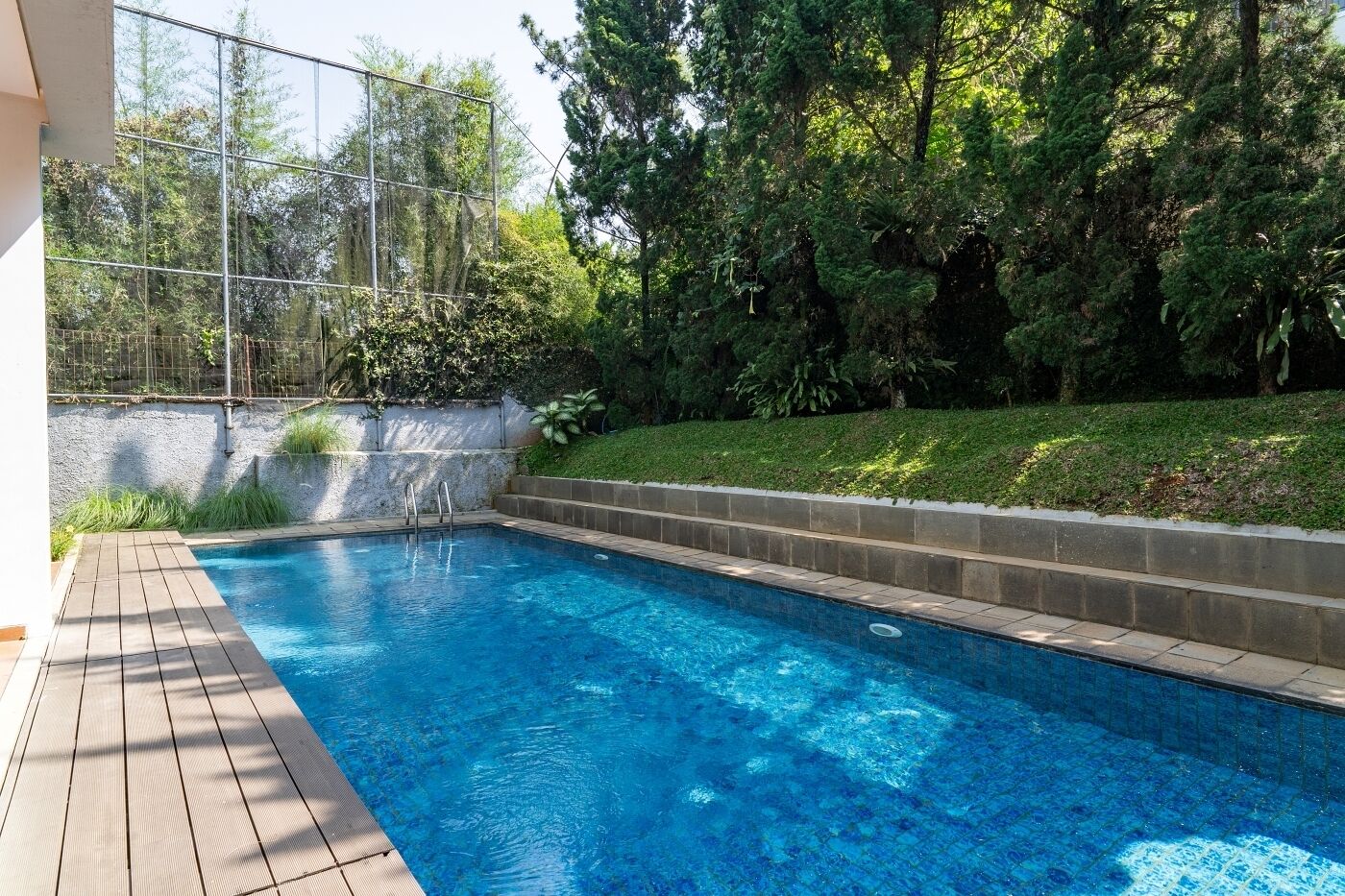 A rectangular swimming pool with a tiled edge, surrounded by a wooden deck and a stone wall.