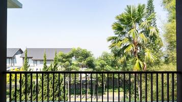 A balcony with a black metal railing, overlooking a residential area with houses and palm trees.