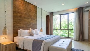 Quarto moderno com cama grande, mesas de cabeceira, um banco e vista para o verde pela janela.