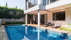 Uma casa moderna com piscina, espreguiçadeiras e um espaço coberto com varanda.