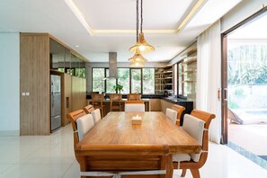 A modern kitchen with a large wooden dining table, built-in cabinets, and a view of the outdoors. - Harmony Hilltop City View 4BR Villa With Pool (Cimenyan)