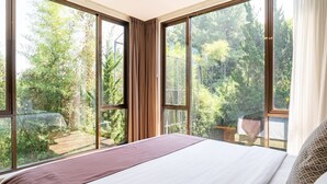 Ein Schlafzimmer mit großem Fenster, einem Bett und Blick auf einen Wald.