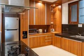 A modern kitchen with wooden cabinets, stainless steel appliances, and a black countertop. - Kirei Mountain View Villa 7 Br With Heated Pool (Bandung)