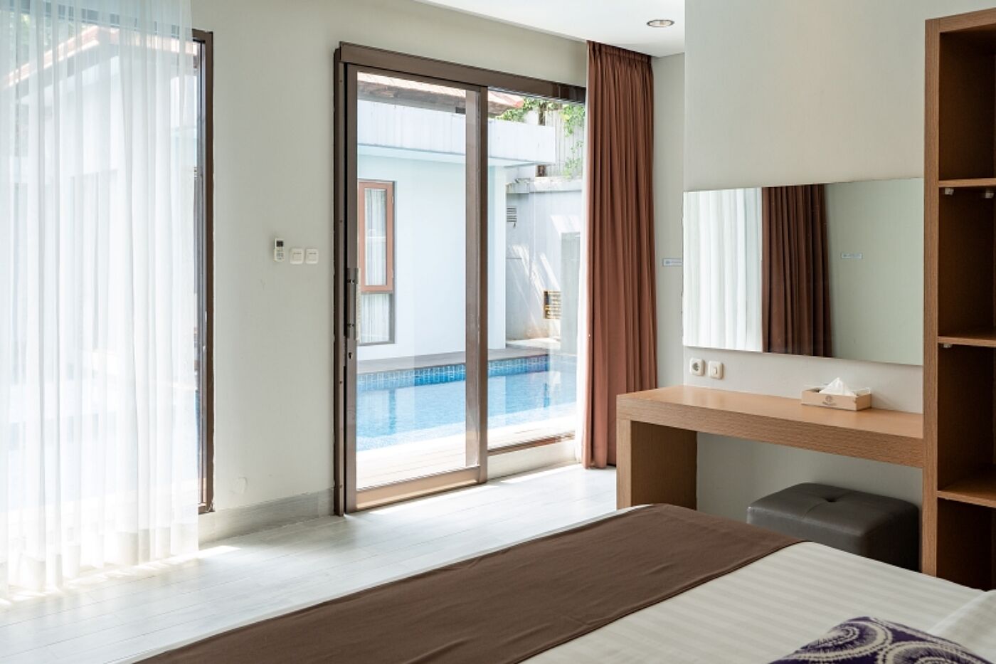 Ein Hotelzimmer mit Bett, Nachttisch, Spiegel und einer Schiebeglastür zum Poolbereich.