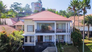 A two-story residential building with a red roof, balconies, and a garden area.