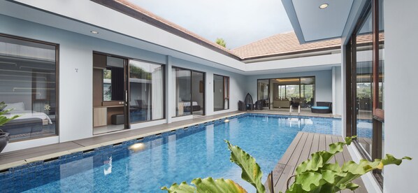 Una piscina interior moderna con paredes de vidrio, una terraza de madera y vistas del entorno.