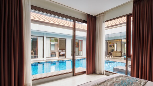 A hotel room with a large window overlooking a swimming pool, a bed with a patterned bedspread, and a view of the pool area.