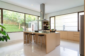 Una cocina moderna con una isla central, taburetes de bar y ventanas amplias que dan a zonas verdes.